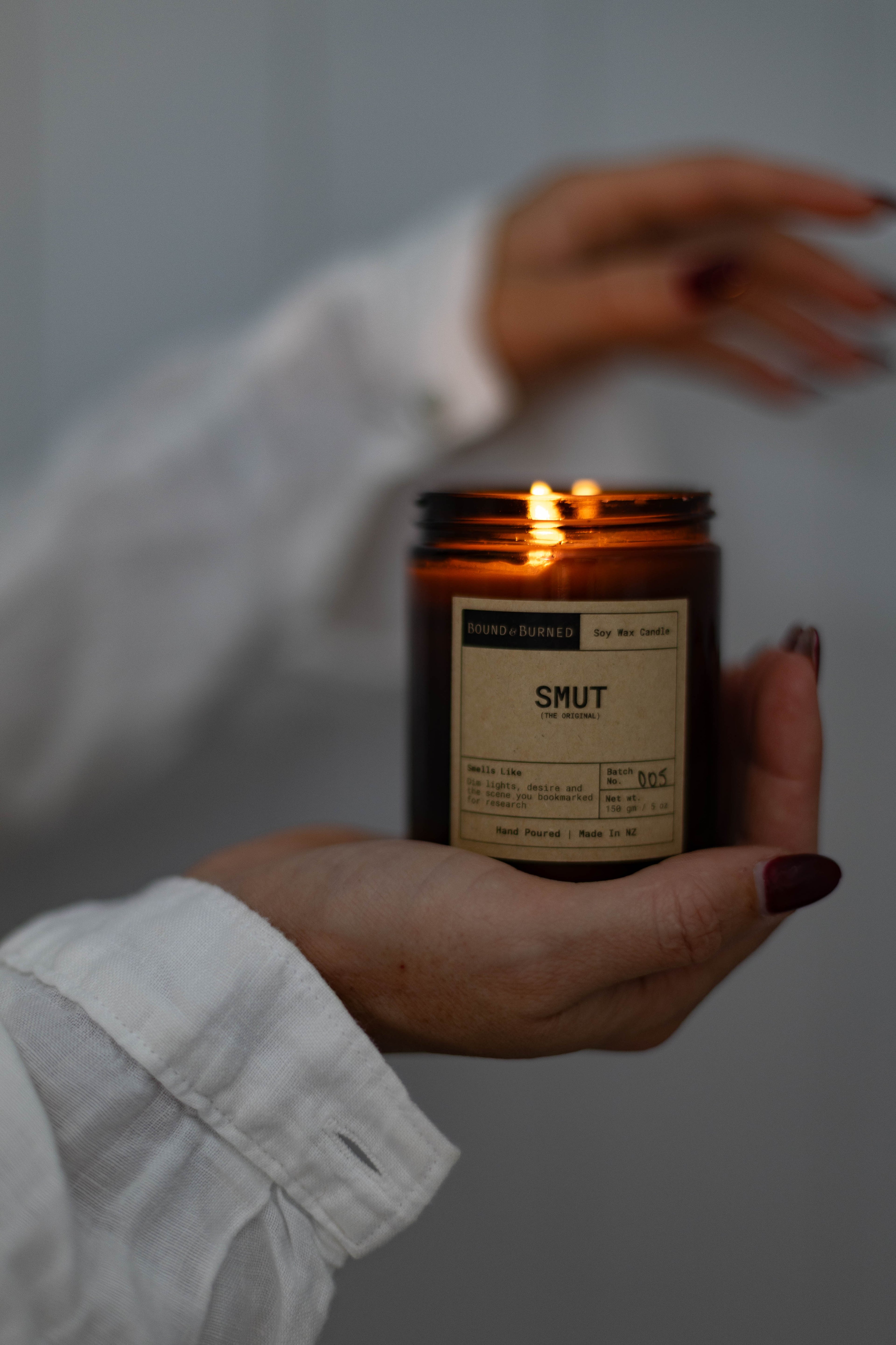 Hand holding a lit candle labeled 'SMUT' against a neutral background