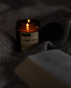 Candle labeled 'Cowboy Smut' on a textured surface with warm glow