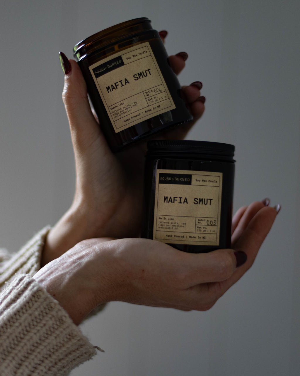 Hands holding two small jars labeled 'Mafia Smut' against a plain background