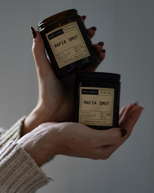 Hands holding two small jars labeled 'Mafia Smut' against a plain background